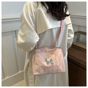 Pink crossbody camera bag with silver liquid butterfly detail worn on a white trench coat