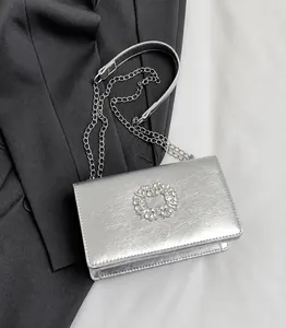 Detail of silver metallic textured crossbody bag with a round rhinestone buckle