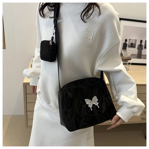 Detail of black pleated crossbody bag featuring a silver metal butterfly and round pouch