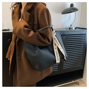 Detail of elegant black leather tote bag with white branded strap on shoulder of a model