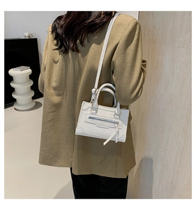 Detail view of a white mini handbag with long tassels and crossbody strap on a model