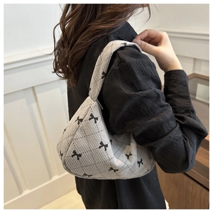 Détail d'un sac à main gris en velours côtelé avec nœuds, porté comme sac sous le bras
