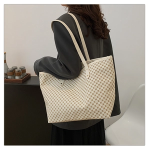 Detail view of large cream tote bag with brown square pattern on a shoulder strap
