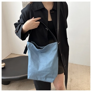 Détail du sac seau en denim bleu clair avec bandoulière noire et texture minimaliste épurée