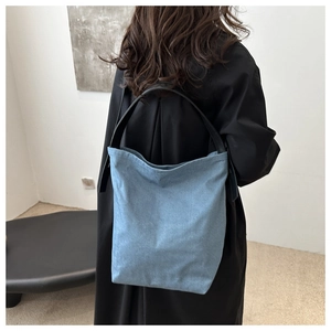Détail d'un sac seau en denim bleu marine avec anses en cuir noir porté par un mannequin
