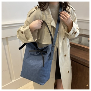 Sac seau en denim bleu avec bandoulière réglable en cuir sur un trench-coat beige