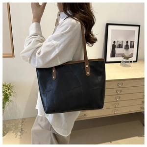 Dettaglio di una grande borsa tote nera con cuciture geometriche e spalline in pelle marrone