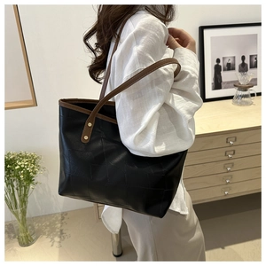 Dettaglio di una grande borsa tote in pelle nera con manici marroni e rivetti in metallo
