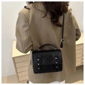 Detalle del bolso bandolera negro con costuras de corazón y lazo usado por una modelo