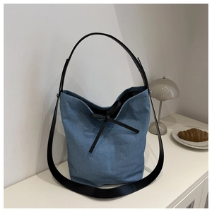 Sac seau en denim bleu avec bandoulière en cuir noir et nœud sur une surface blanche