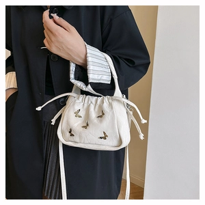 Close-up of white drawstring bucket bag with textured leather and gold butterfly details