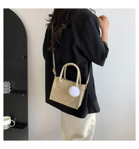 Detailansicht beige gesteppte Handtasche mit Plüsch-Anhänger von Model getragen im Raum