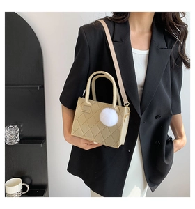 Detail der beige gesteppten Mini-Tasche mit weicher Textur und weißem Plüschanhänger