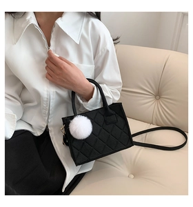 Detail der schwarzen gesteppten Mini-Handtasche mit flauschigem weißem Bommel-Anhänger