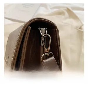 Detailed close-up of premium metal hook and yellow contrast stitching on vintage brown bag