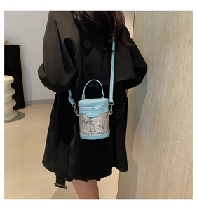 Détail du sac seau en maille bleu clair à motifs plumes porté sur un manteau noir