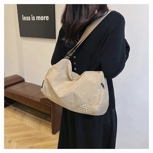 Détail du sac bandoulière en nylon beige à texture froissée et logo blanc brodé