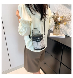 Detail of grey patterned bucket bag with black leather trim and crossbody strap