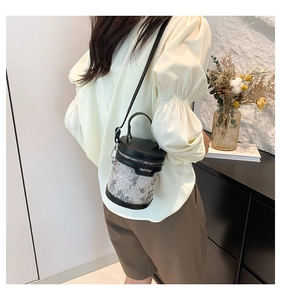 Détail d'un sac seau brodé gris avec coutures en cuir noir et bandoulière réglable