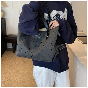Bolso tote grande gris oscuro con estampado de estrellas y asas de cuero al hombro del modelo