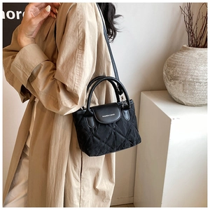 Detail of black quilted crossbody bag with 'FASHION & BAGS' text on beige trench coat