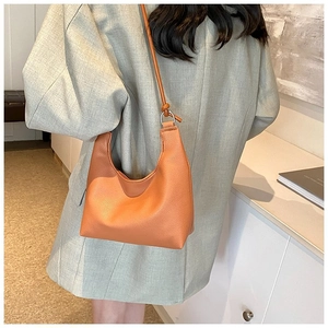 Détail d'un sac à bandoulière en cuir orange porté par un mannequin dans un décor épuré