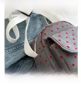 Detail of dark grey canvas bag with red heart patterns and white shoulder strap buckle