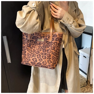 Fashionable leopard print tote bag with brown leather handles worn by a model in casual style