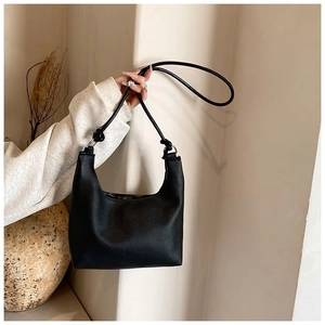 Detalle de bolso negro de cuero PU con textura granulada y hebillas metálicas plateadas
