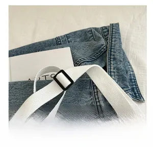 Detail of adjustable white woven strap with black buckle on a denim shoulder bag