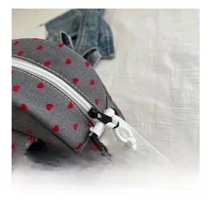 Close-up of grey canvas shell bag featuring red heart patterns and smooth white zipper