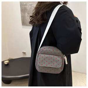 Detail of dark grey canvas crossbody bag with red heart pattern and white woven strap