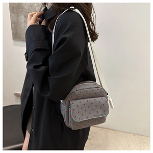 Close-up of grey canvas shoulder bag with red heart pattern and wide white strap