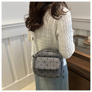 Close-up of gray quilted crossbody bag with black polka dots and white braided rope zipper pull