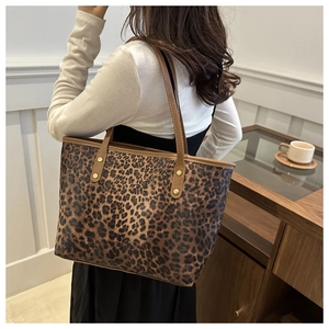 Detailed view of leopard print tote bag with brown leather handles and gold rivet studs