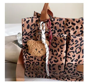 Detail of leopard print tote bag with plush bear charm and woven rope accessories