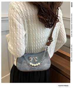 Detail of light blue denim shoulder bag with silver bow and pearl chain on a model