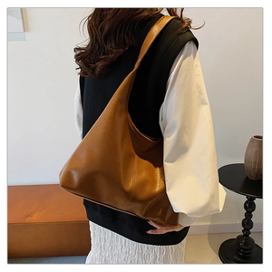 Detail of a large brown faux leather tote bag with a smooth finish and minimalist stitching