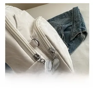 Detail view of smooth dual metal zippers on a white crinkled fabric crossbody chest bag