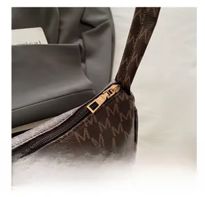 Detail of smooth gold zipper and retro M-letter pattern on dark brown crescent bag