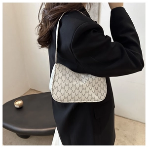Close-up of a white crescent shoulder bag with 'M' monogram print worn over a black blazer
