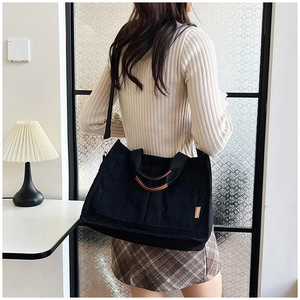 Detailed view of black corduroy tote bag featuring a fashion tag and shoulder straps