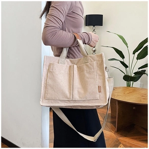 Detail of beige corduroy tote bag with front pockets and fashion tag worn by model
