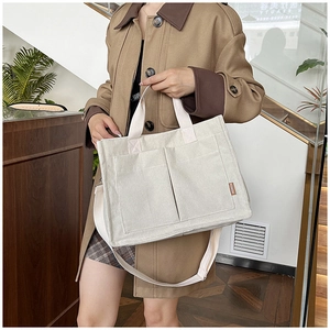 Close-up of off-white corduroy tote bag with dual outer pockets and long shoulder strap