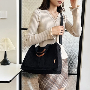 Large black corduroy tote bag with brown leather handles and adjustable shoulder strap
