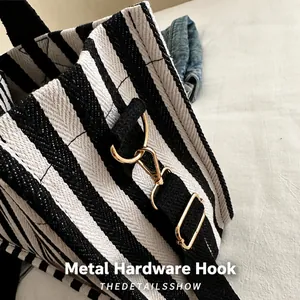 Detail of the golden metal hook and adjustable strap on a striped canvas tote bag