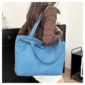 Sky blue denim tote bag with zipper closure shown on shoulder for size reference