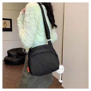 Detail of black nylon crescent crossbody bag with white pompom charm and adjustable strap