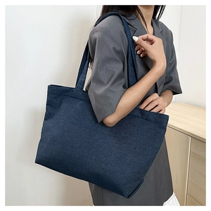 Detail view of deep blue denim tote bag with large capacity worn with a casual blazer