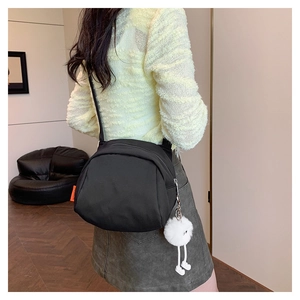Detail of black nylon crossbody bag featuring a cute plush pendant and fashion label